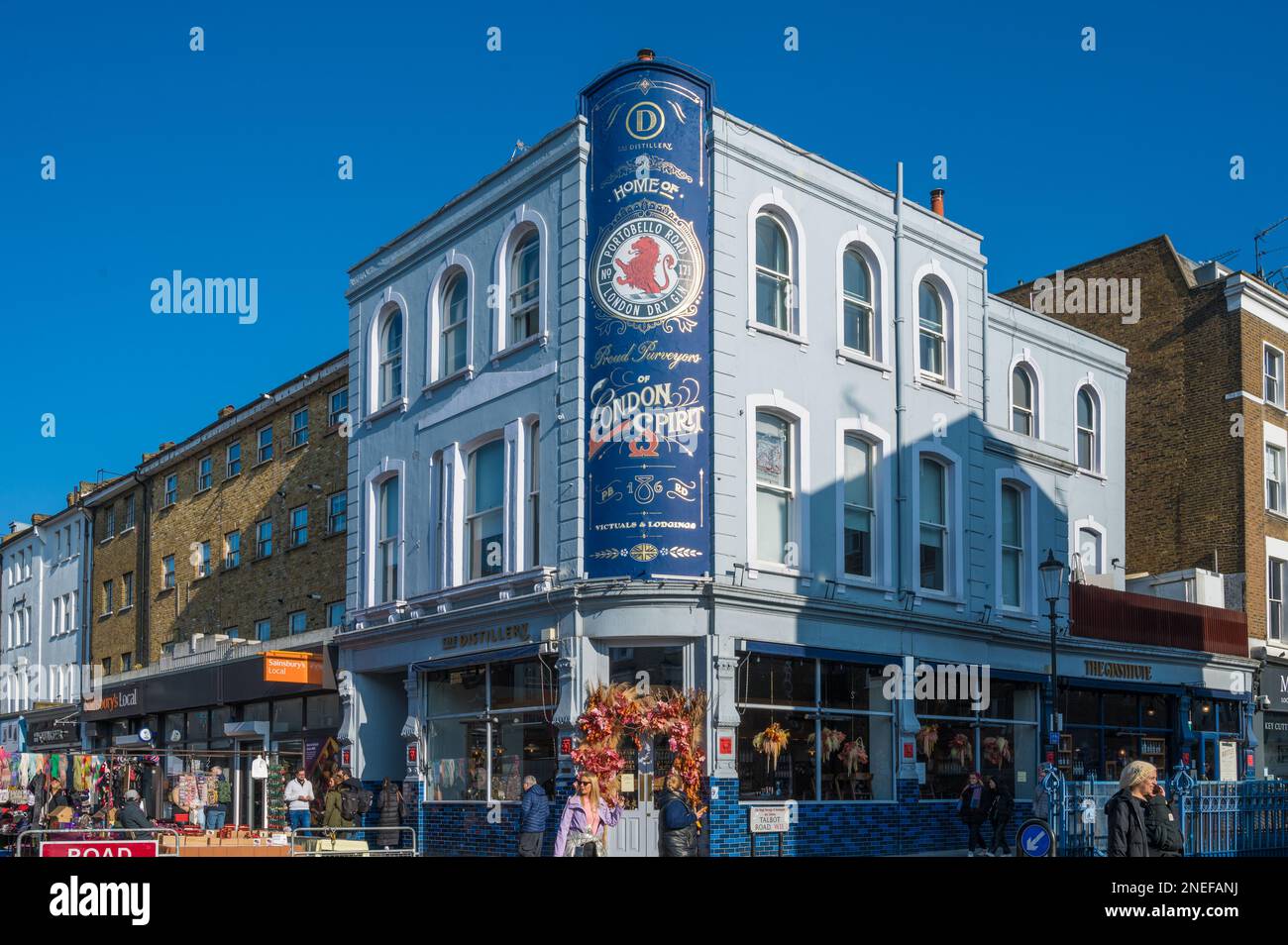 People out and about on a sunny day, Portobello Road. Colourful facade of The Distillery hotel