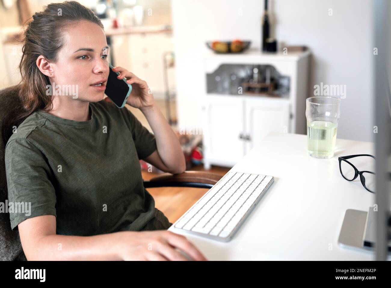 Young woman working from home working on computer and talking cell phone. Stock Photo
