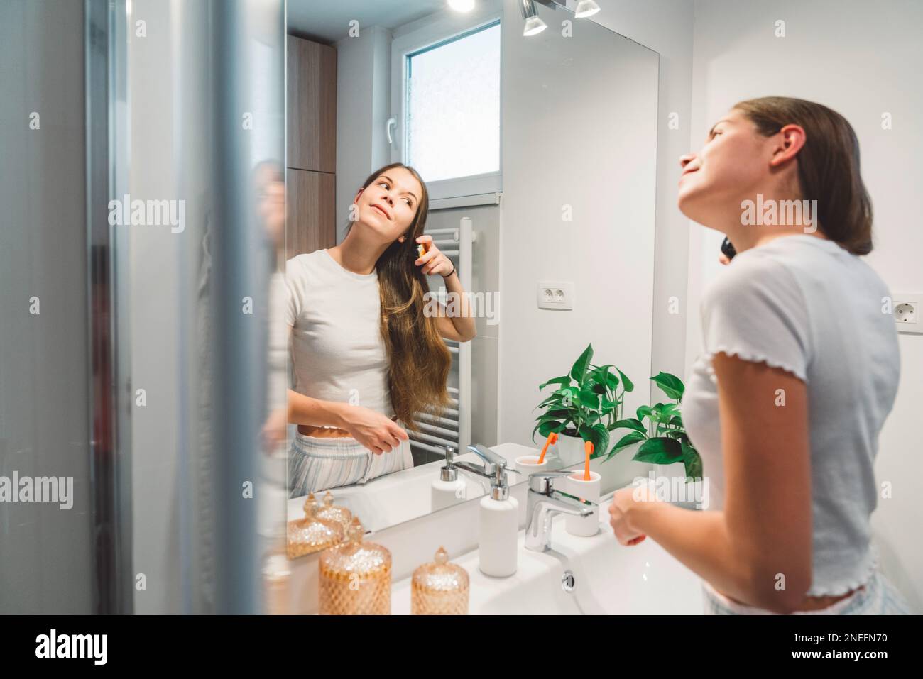 Side view of a woman brushing her long brown hair while looking at herself in the mirror  Stock Photo