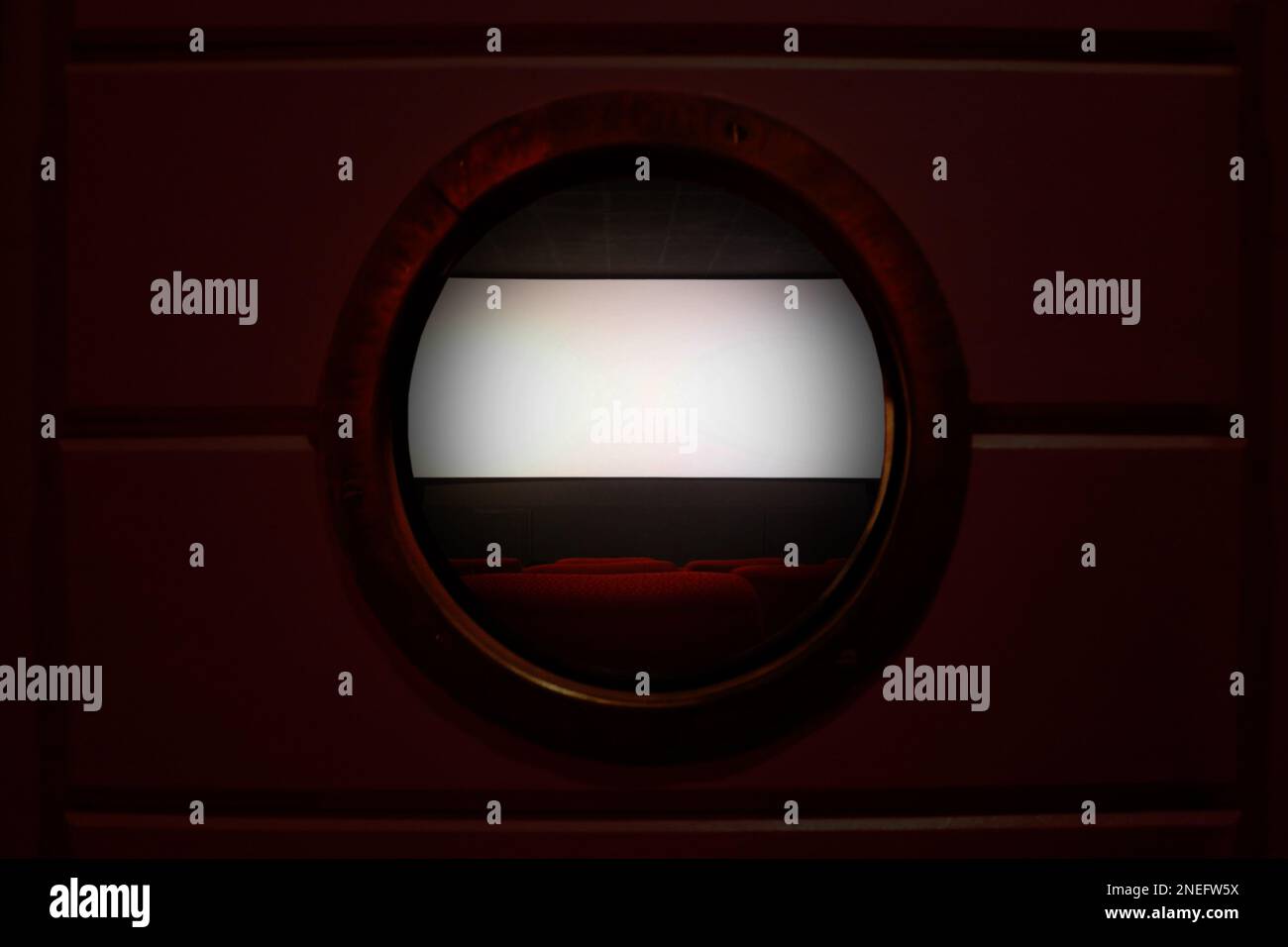 Row of empty red seats in a movie theater with the white projection screen in the background few minutes before the movie begin. The room is seen behi Stock Photo