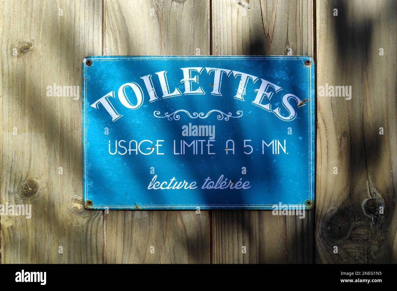 Blue laminated metal plate with a humorous text stating in French 'Toilettes, usage limité à 5 minutes. Lecture tolérée.', meaning in English 'Toilets Stock Photo