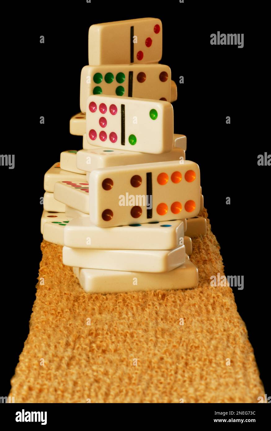 Dominoes with colorful dots are stacked high in a pile on a coco mat material. Isolate image has room for text. Tiles are clean and new. Stock Photo