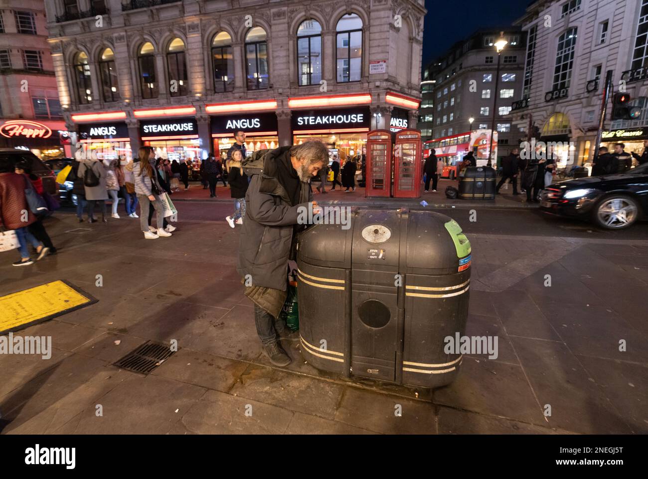 A homeless man searches a street refuse bin for any food on the streets