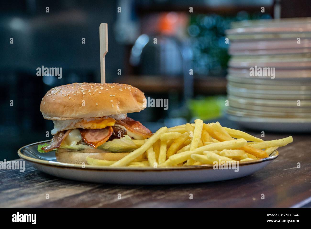 A tasty looking fully loaded beef burger served alongside French Fries eye level Stock Photo