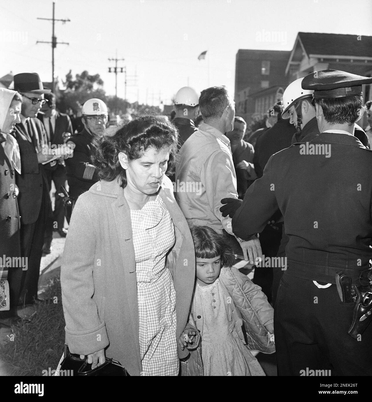 Women crowd sidewalk and jeer as Mrs. James Gabrielle, with police escort  walks her daughter home in New Orleans on Nov. 30, 1960, after day in  integrated William Frantz School. Few white