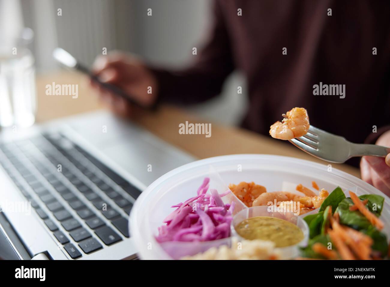 Close Of Man Eating Healthy Lunch At Office Deak Whilst Using Laptop Stock Photo