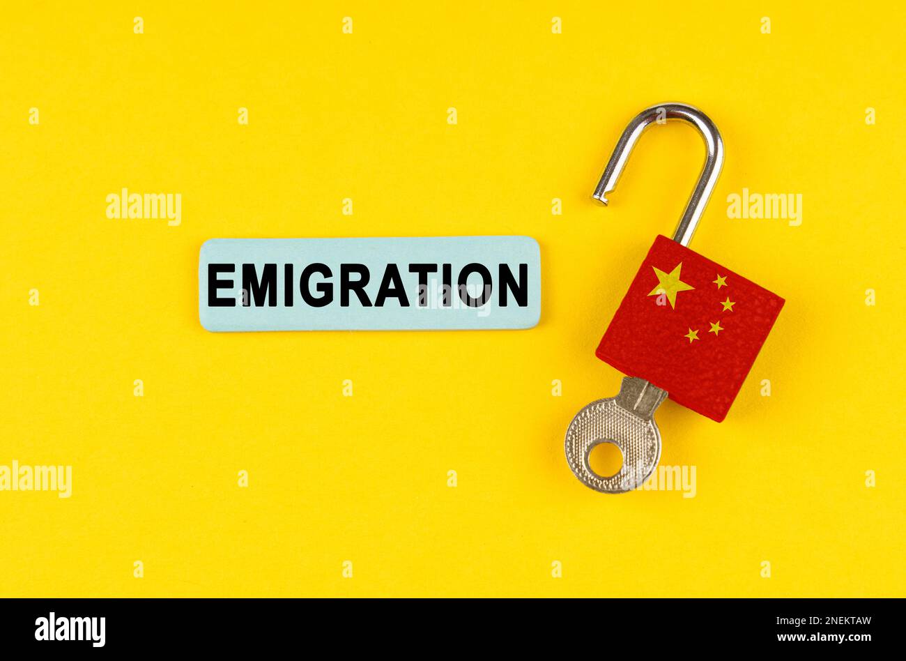 On a yellow surface, an open lock with the image of the flag of China and a sticker with the inscription - Emigration Stock Photo
