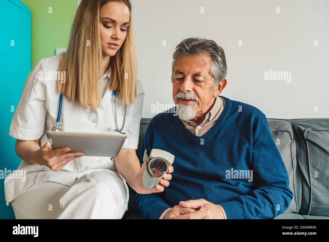 Blonde nurse assisting senior man at home, taking all his vitals Stock Photo