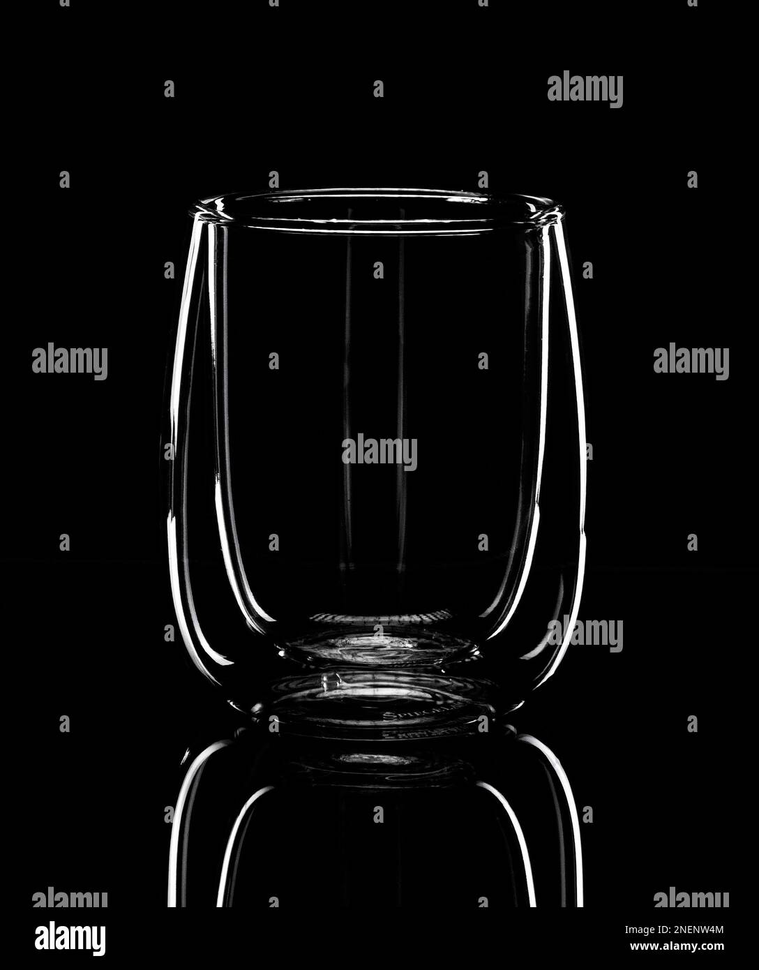 Minimalism, the luminous silhouette of a glass for latte is reflected in a black mirror table. Monochrome photo Stock Photo