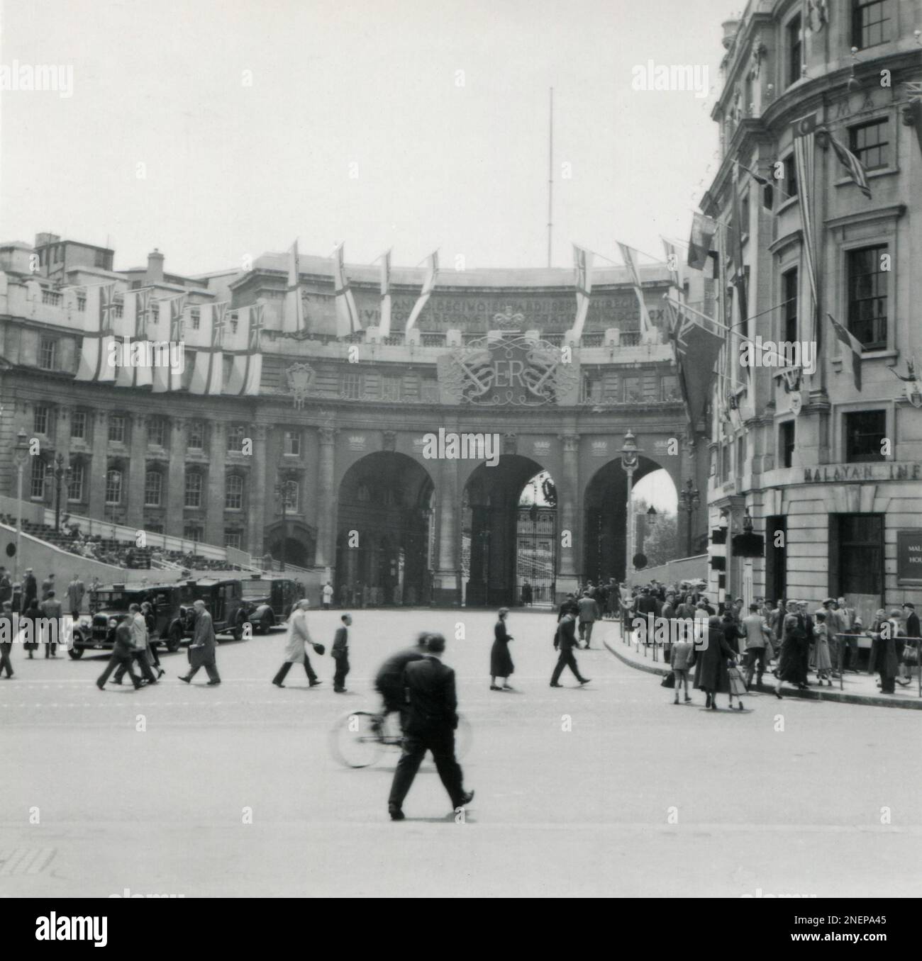 London, England. 1953. A view of Admiralty Arch from The Mall, near Trafalgar Square. The Arch is decorated with a large Royal Cypher and Royal Ensign flags, especially for the coronation of Queen Elizabeth II, which took place on 2nd June 1953. In preparation for the procession, a temporary stand had been erected adjacent to the arch. In the foreground is Malaya House, which has been decorated with flags. Stock Photo