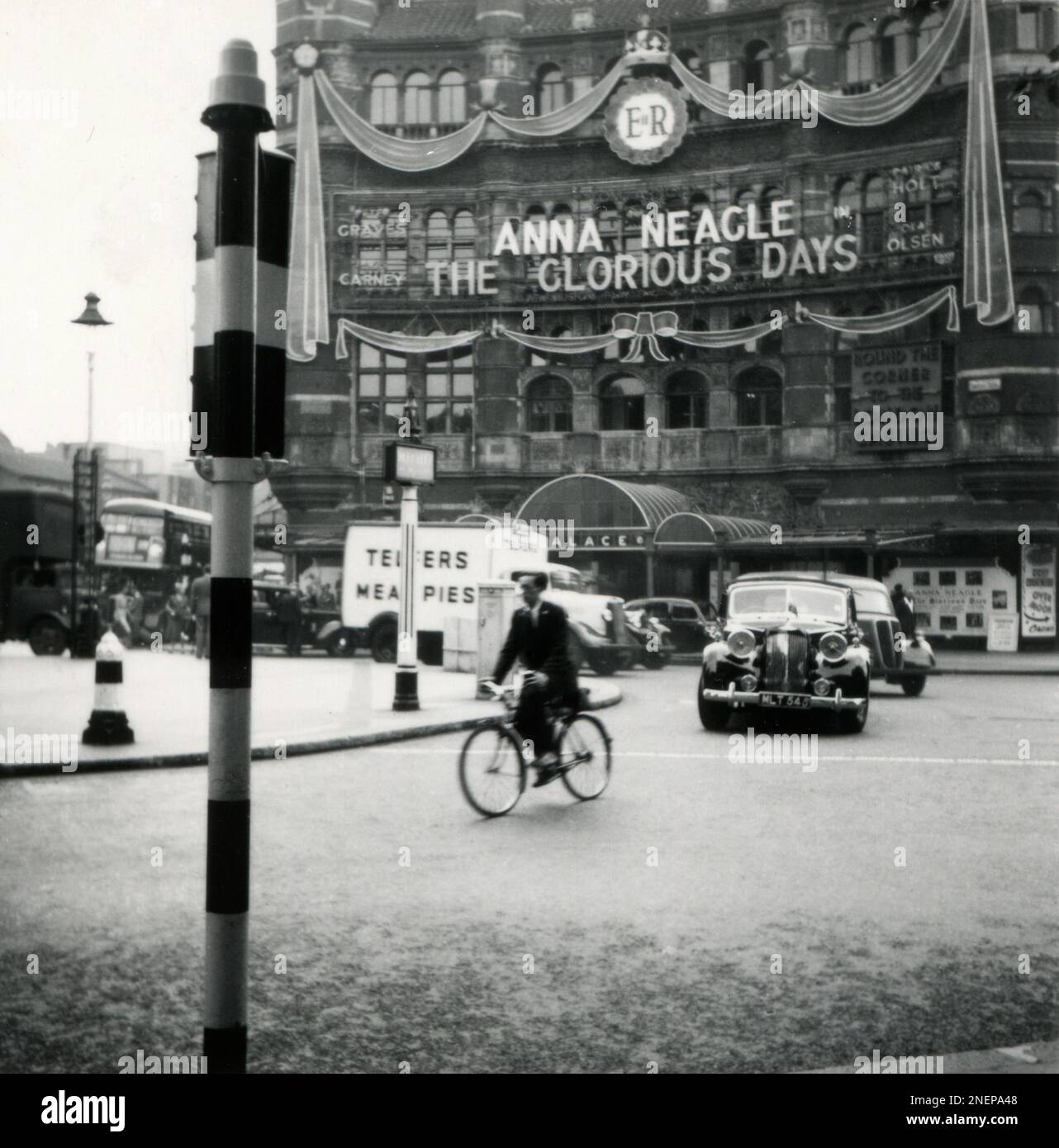 London, England. 1953. A view of The Palace Theatre in London’s West End, taken from the junction of Charing Cross and Cambridge Circus. The theatre has been decorated with a large Royal Cypher and faux ribbons, especially for the coronation of Queen Elizabeth II, which took place on 2nd June 1953. Showing at the theatre is the musical, ‘The Glorious Days’, starring Anna Neagle. Stock Photo