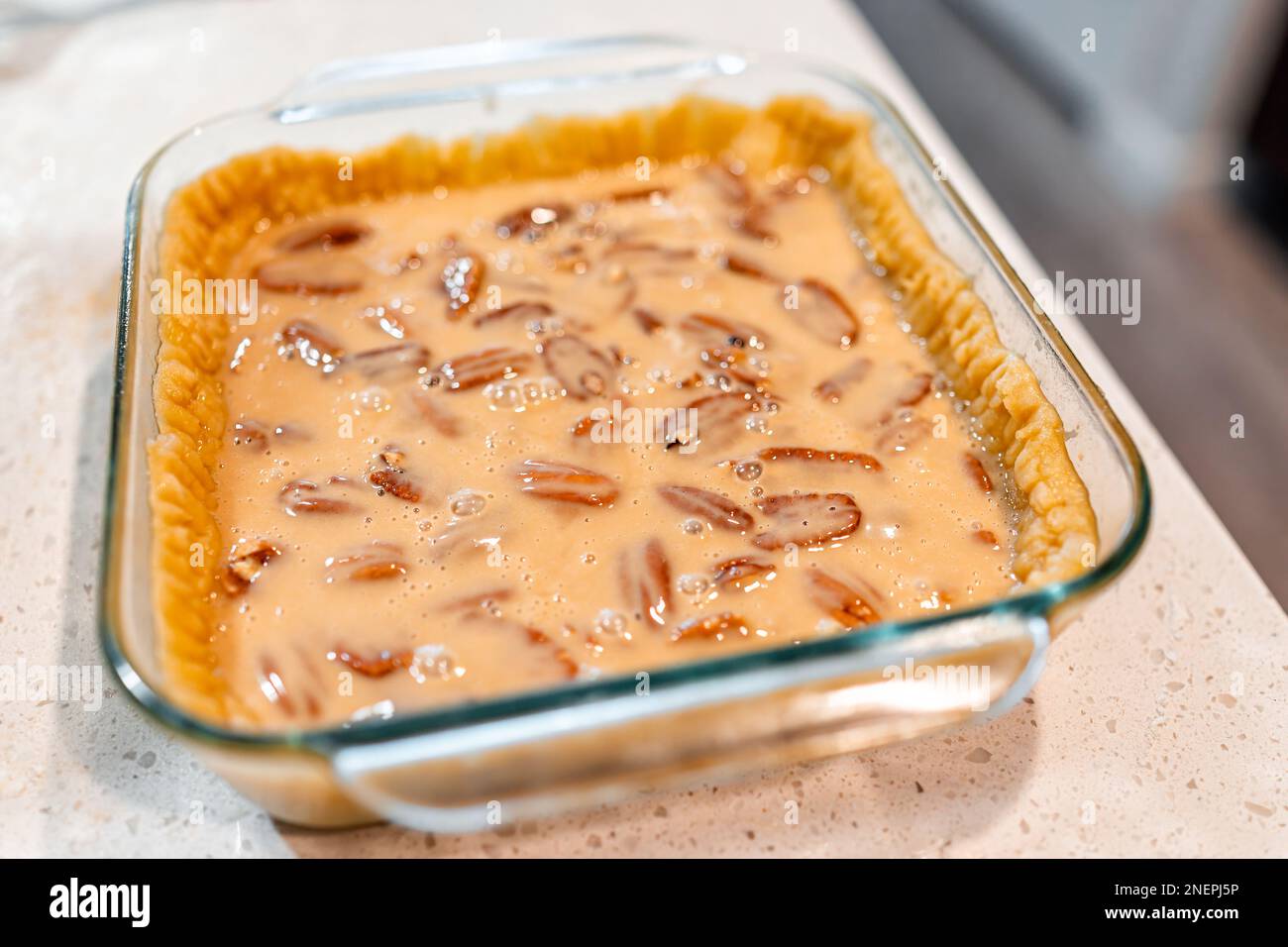 Closeup of pecan pie in glass pan with homemade crust and raw sweet
