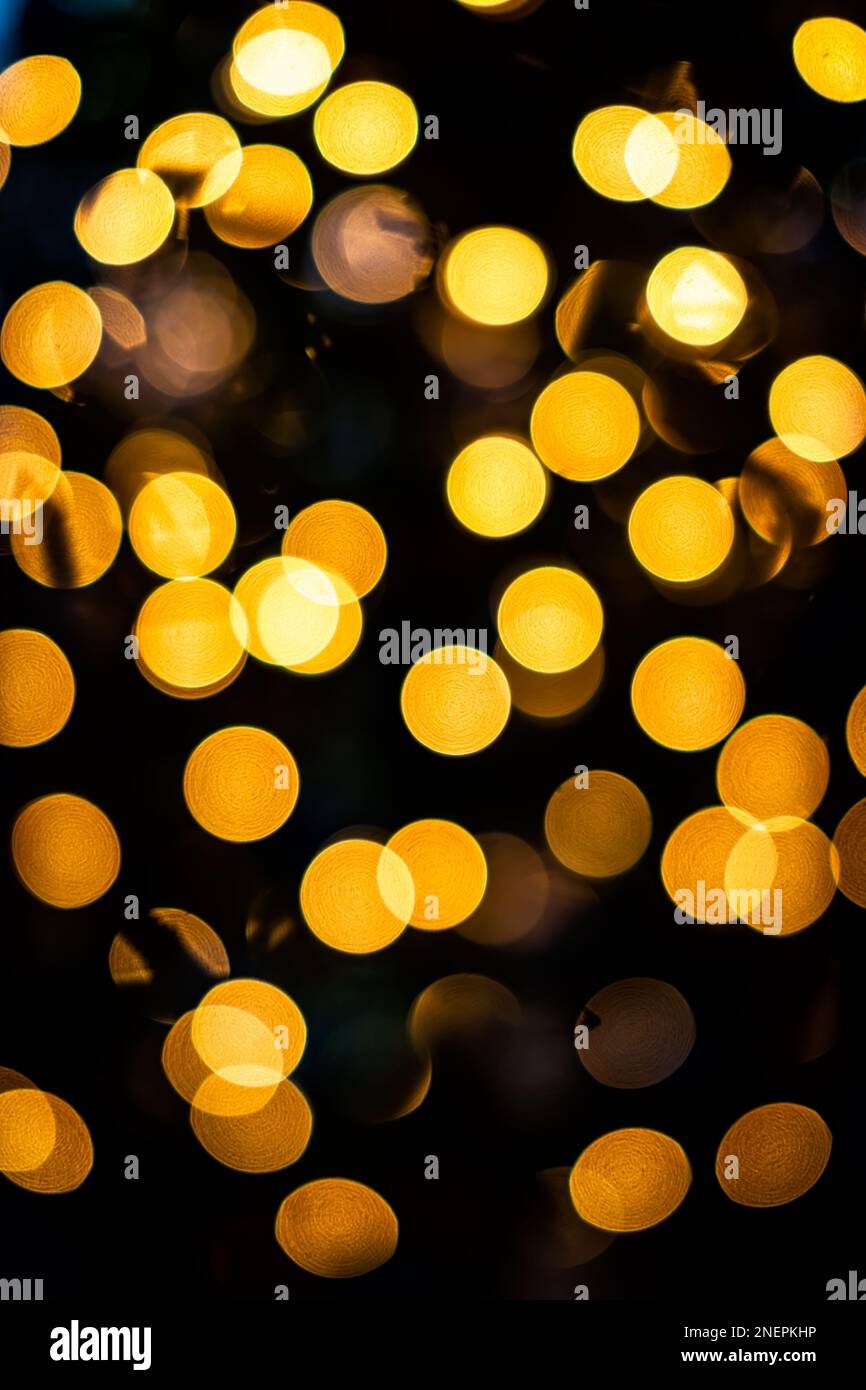 Golden yellow bokeh circles vertical view from New Year Christmas tree lights illuminations with defocused blurred view at night and black background Stock Photo