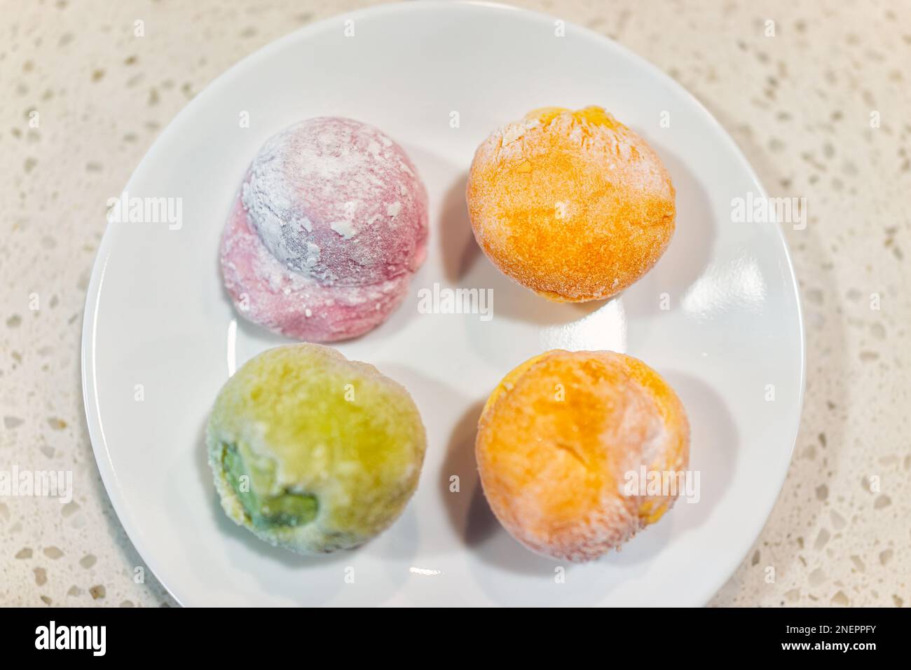 Ice cream mochi daifuku dessert, sweet Japanese food on white plate macro closeup of four frozen filled rice cake of green tea matcha, strawberry mang Stock Photo