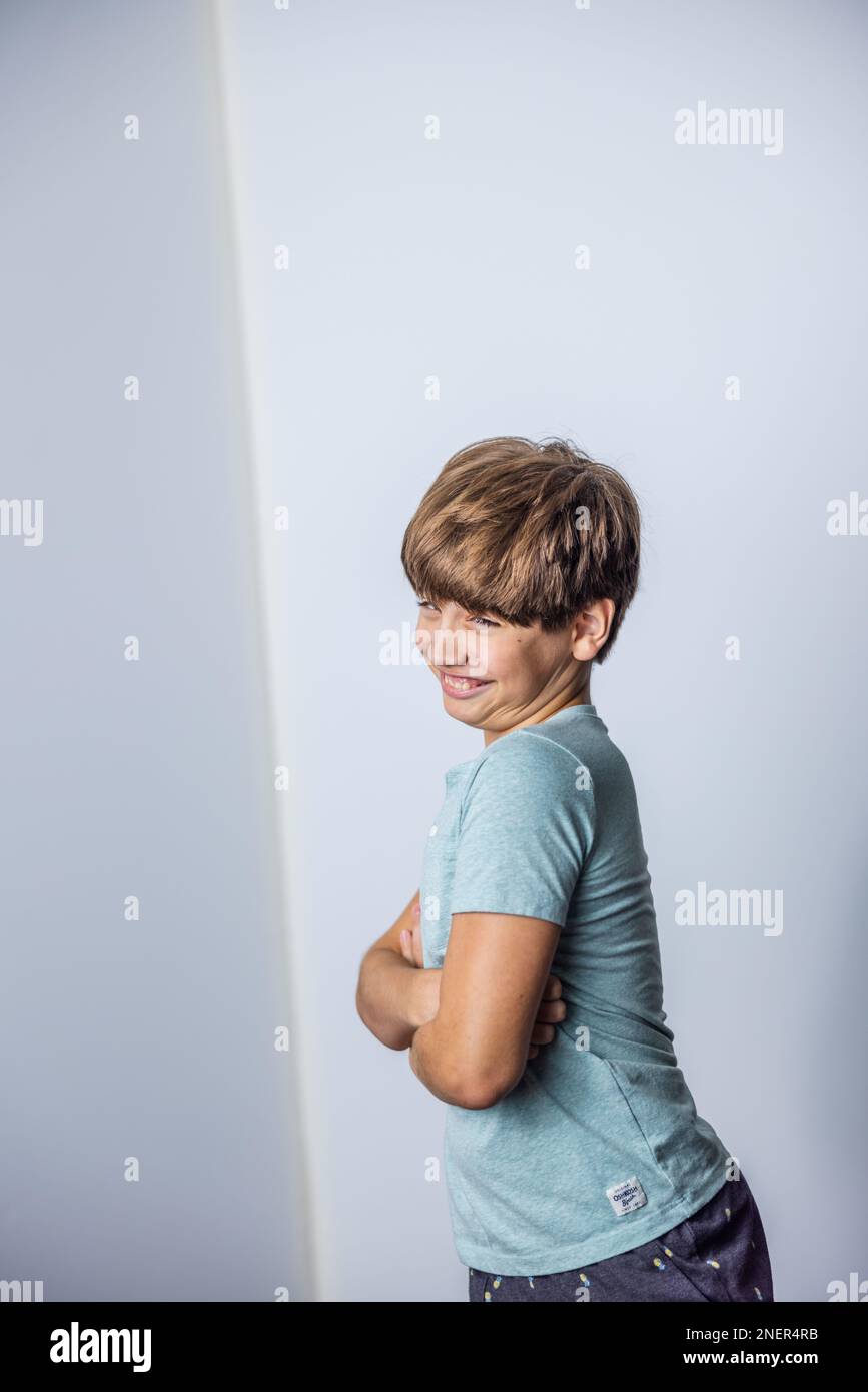 A pre-teen tween boy with his arms crossed being silly standing near a corner with white walls with copy space Stock Photo