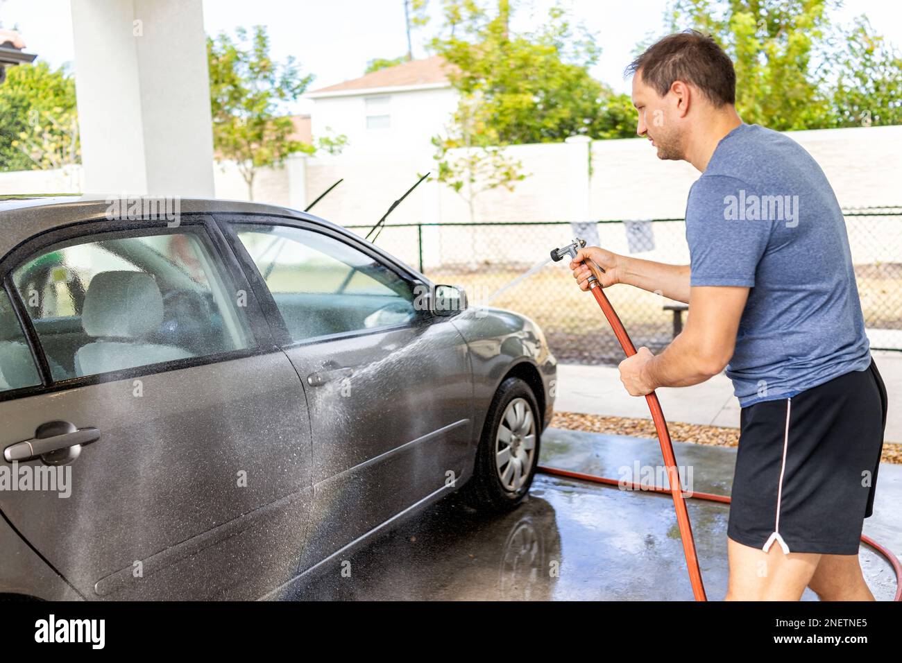 Man washing vehicle at car wash selfservice station, spraying water with sprayer hose outside