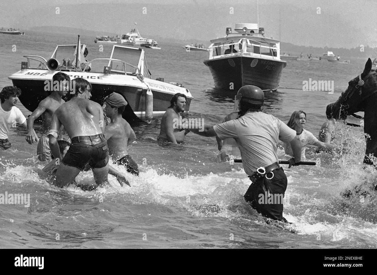 A policeman charges into the water, Aug. 10, 1975 at Carson Beach in  Boston, in pursuit of bathing demonstrators. Black and white bathers threw  rocks and bricks at one another. About 500