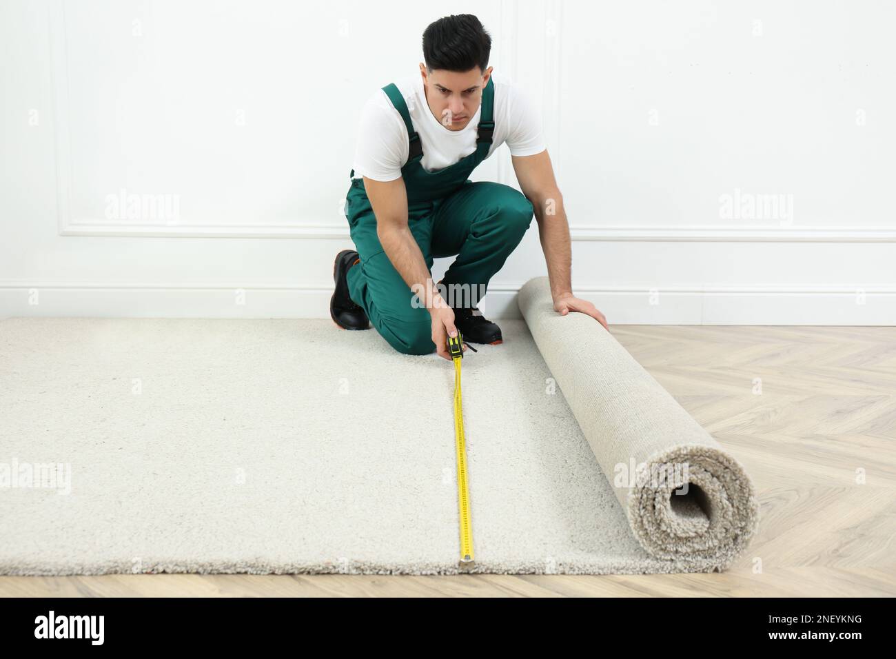Worker with measuring tape installing new carpet indoors Stock Photo