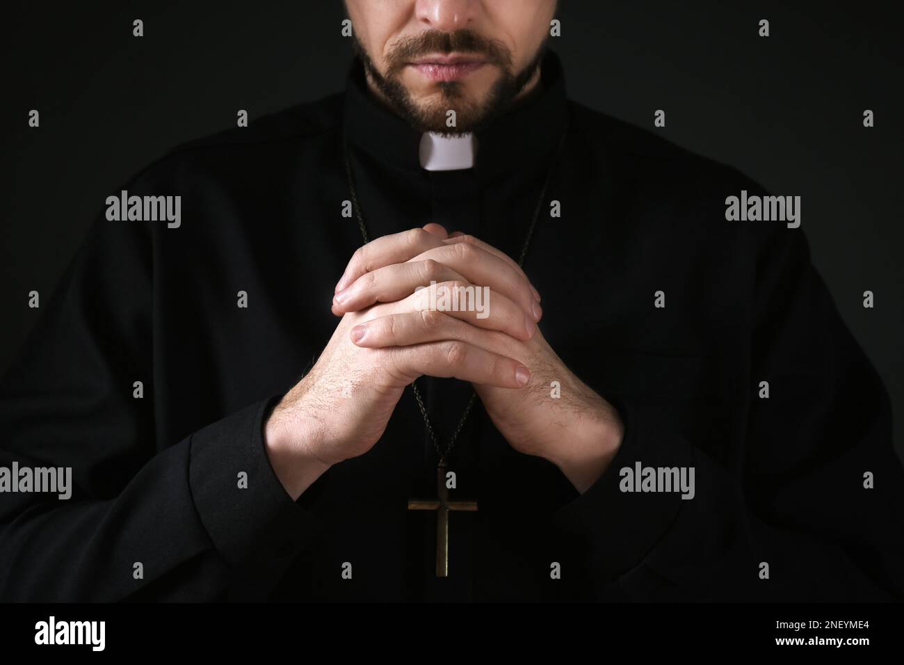 Priest in cassock praying on dark background, closeup Stock Photo