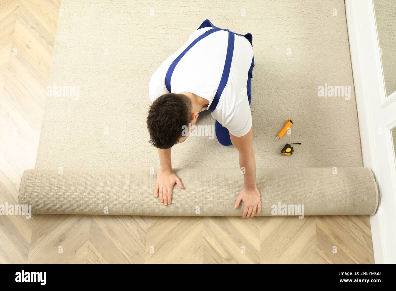 Worker rolling out new carpet flooring indoors, top view Stock Photo