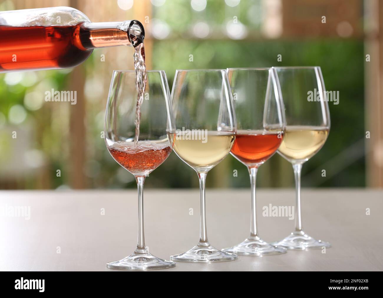 Pouring rose wine from bottle into glass on table against blurred ...