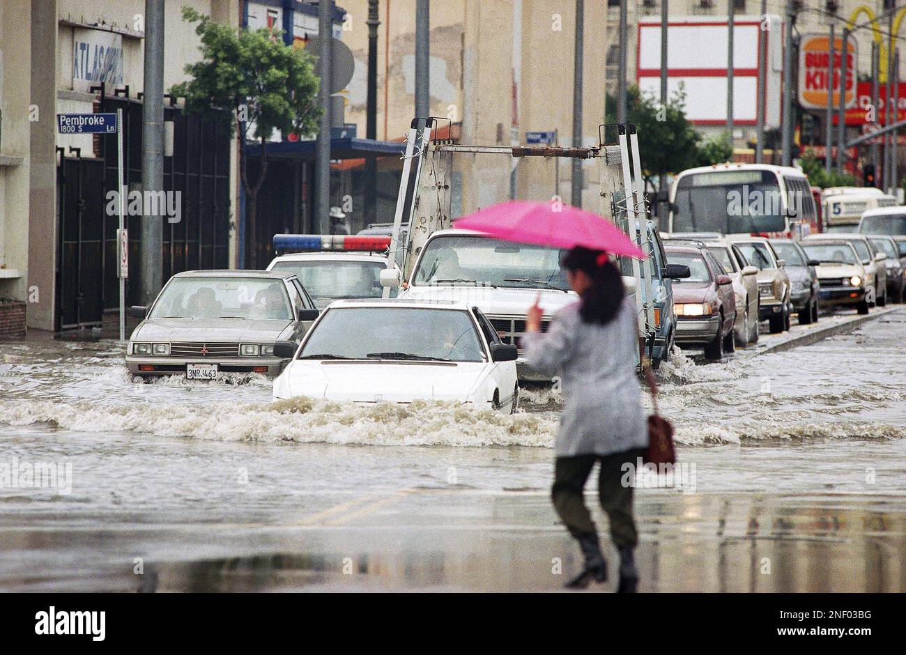 A pedestrian crosses the street as a line of cars bog through a water ...