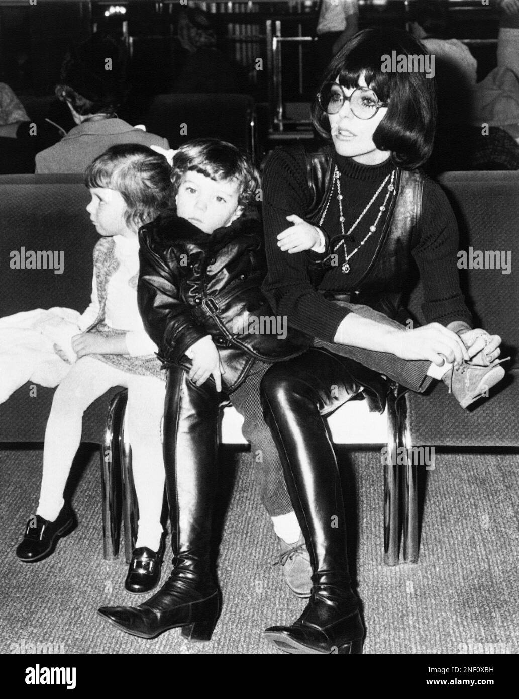 Actress Joan Collins, wearing high leather boots and a leather skirt over  her sweater, laces the shoe of her three-year-old son, Sacha at Heathrow  Airport in London, Dec. 18, 1968. Joan's daughter,