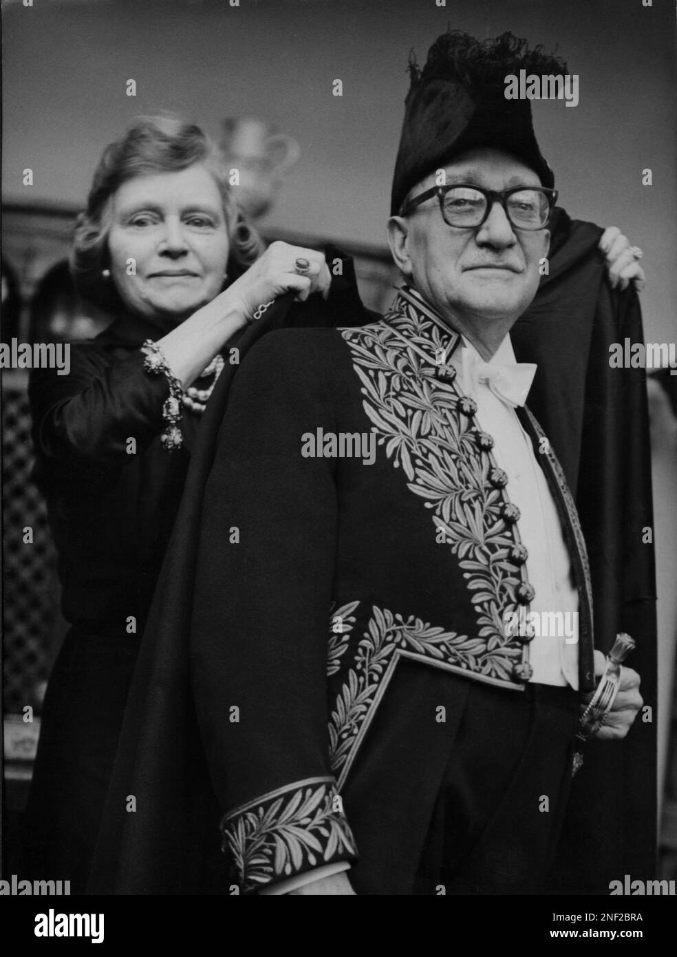 French literary critic Robert Kemp is helped by his wife Yvette Kemp in his  outfit of a member of the Academie Francaise upon becoming a new member of  the French society of