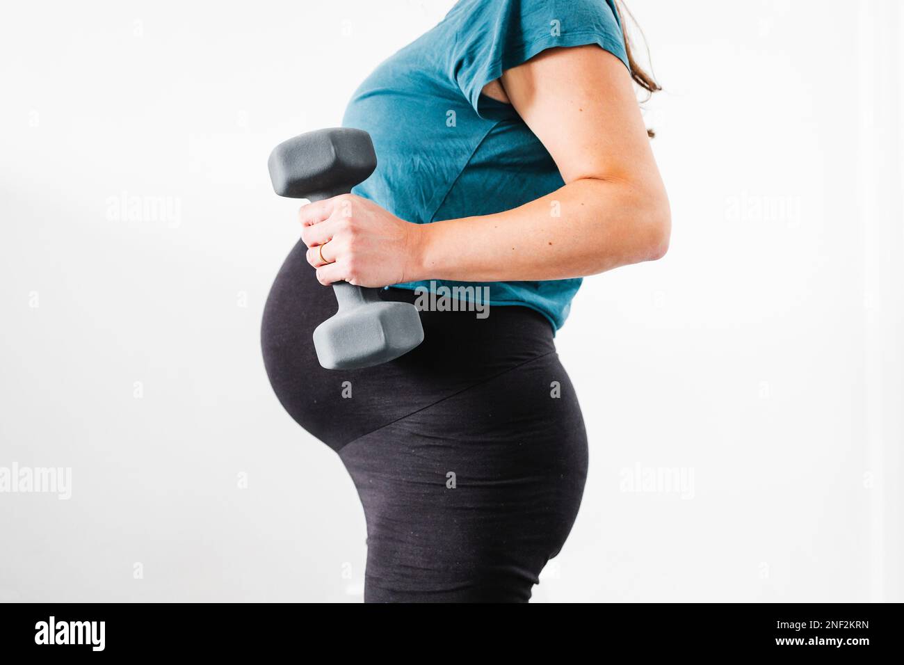 pregnant woman exercising with dumbbell in her hand and showing her bump in the latest stage of pregnancy, mid-section showing the belly and body shap Stock Photo