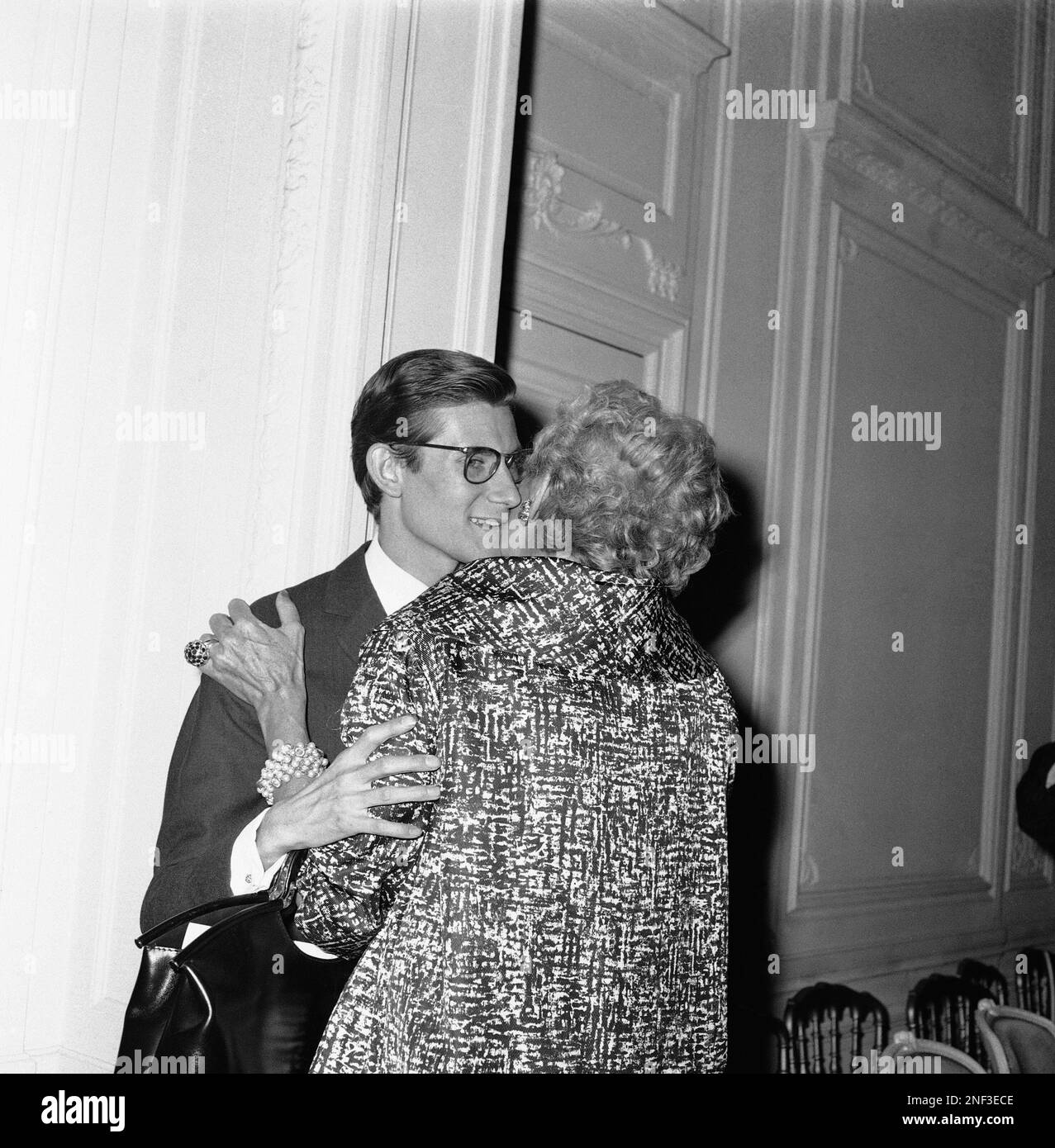 Designer Yves Saint Laurent left of the Paris Fashion House of Dior gets a kiss from Mrs. Alex Lieberman of New York wife of a magazine publisher after the July 30 premiere