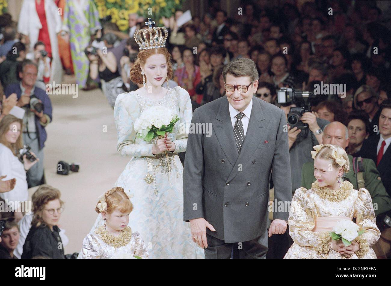French fashion designer Yves St. Laurent, center, acknowledges applause from  spectators as he walks with model in wedding dress and young attendants at  the end of his 1995 fall-winter haute couture show,