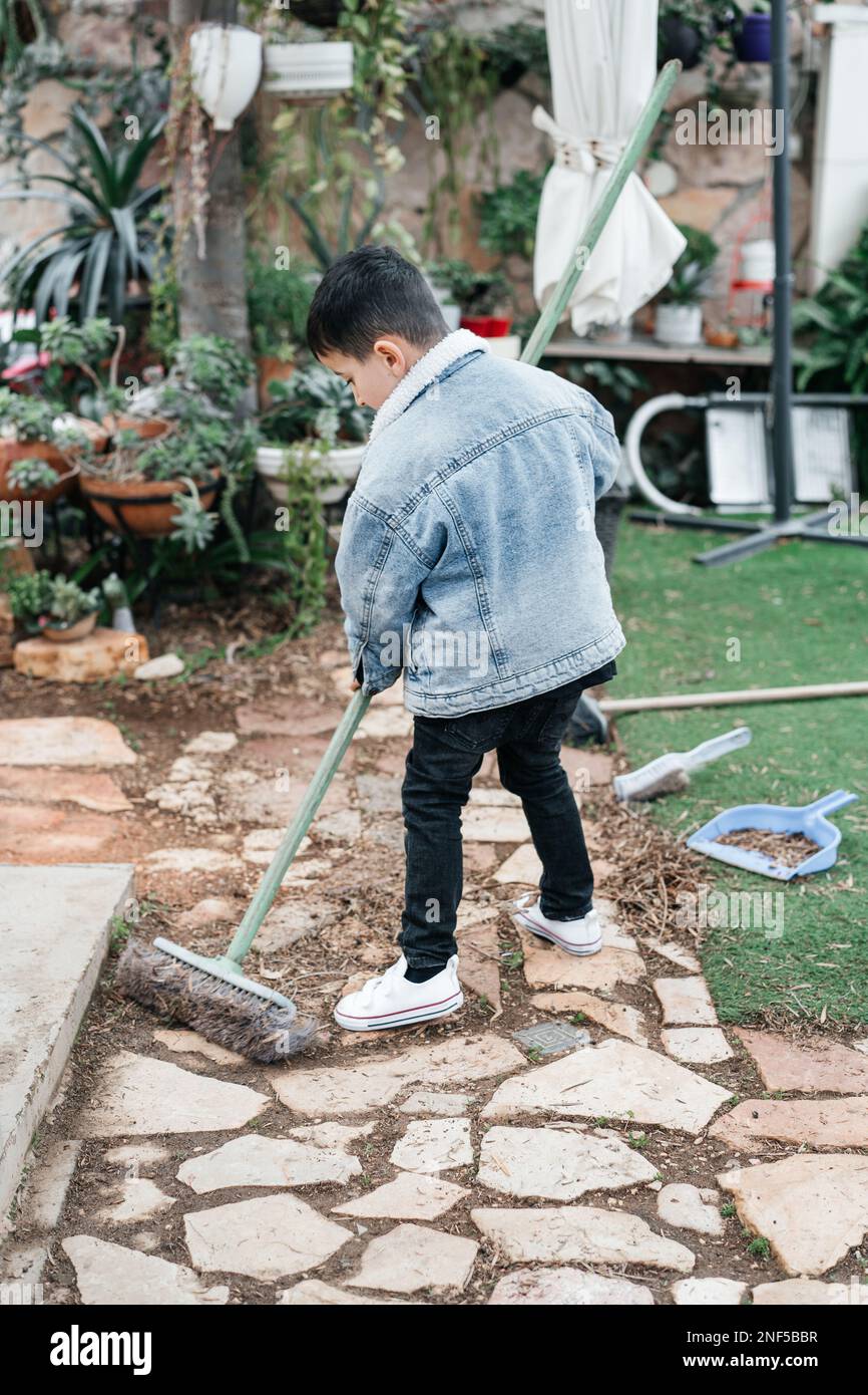 Little child raking dry leaves in a garden. Back view of cute boy cleaning backyard in springtime. Stock Photo