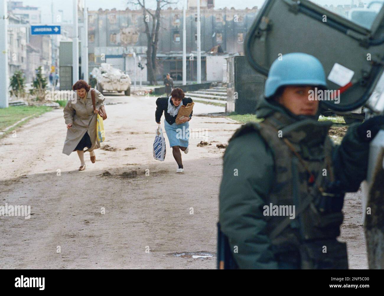 Two residents run along the notorious "Sniper Alley" in Sarajevo trying to evade snipers, April 18, 1995, while a French soldier stands protected by his armored vehicle. Tensions have been high in the Bosnian capital after the killings of two French peacekeepers last week. (AP Photo/Rikard Larma) Stock Photo