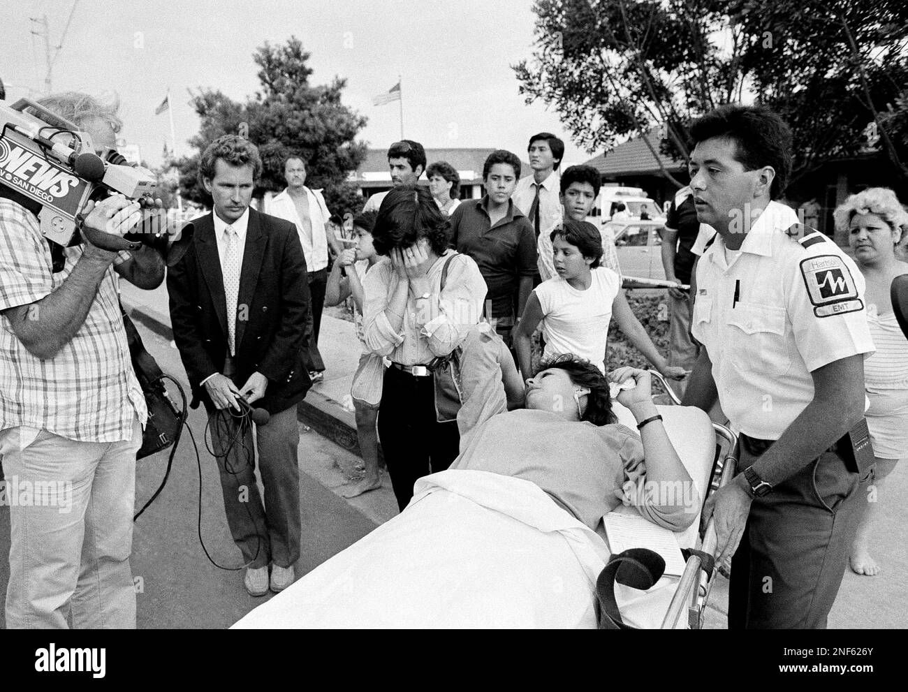 A woman is removed on a stretcher, as a friend covers her face while ...