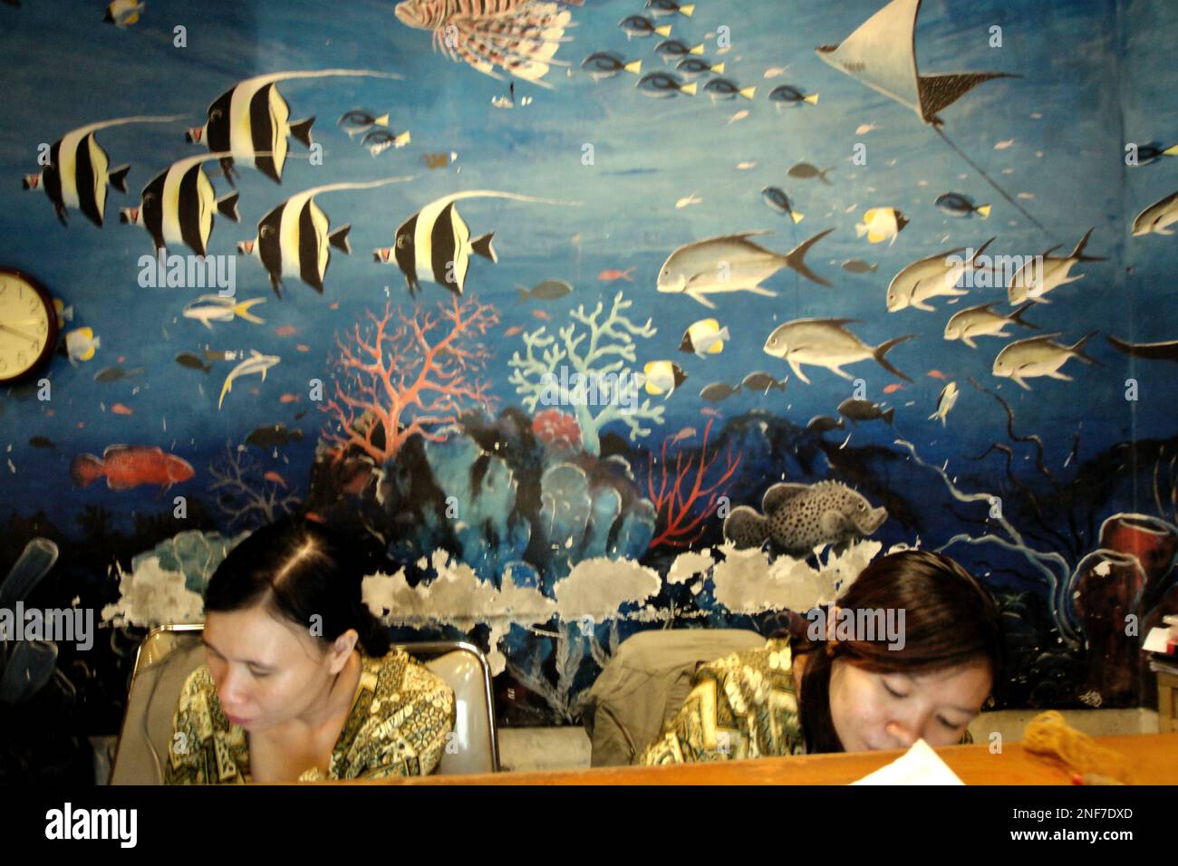 Receptionists respond to a query of a customer at the front desk of a seafood restaurant in Manado, a coastal city and the capital of North Sulawesi province of Indonesia. According to FAO in their latest report called The State of World Fisheries and Aquaculture 2022, Indonesia is the third largest producer of world's fisheries and aquaculture production of aquatic animals. Five countries—China, India, Indonesia, Vietnam, and Peru—are responsible for about 58 percent of the world's production. Indonesia is also one of the countries where aquatic foods contribute half or more of total... Stock Photo