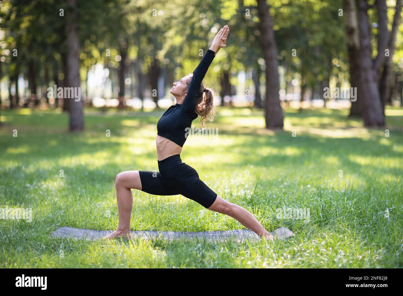 A young woman leading a healthy lifestyle and practicing yoga, performs the exercise of virabhadrasana 1, the pose of a warrior, trains in sportswear Stock Photo