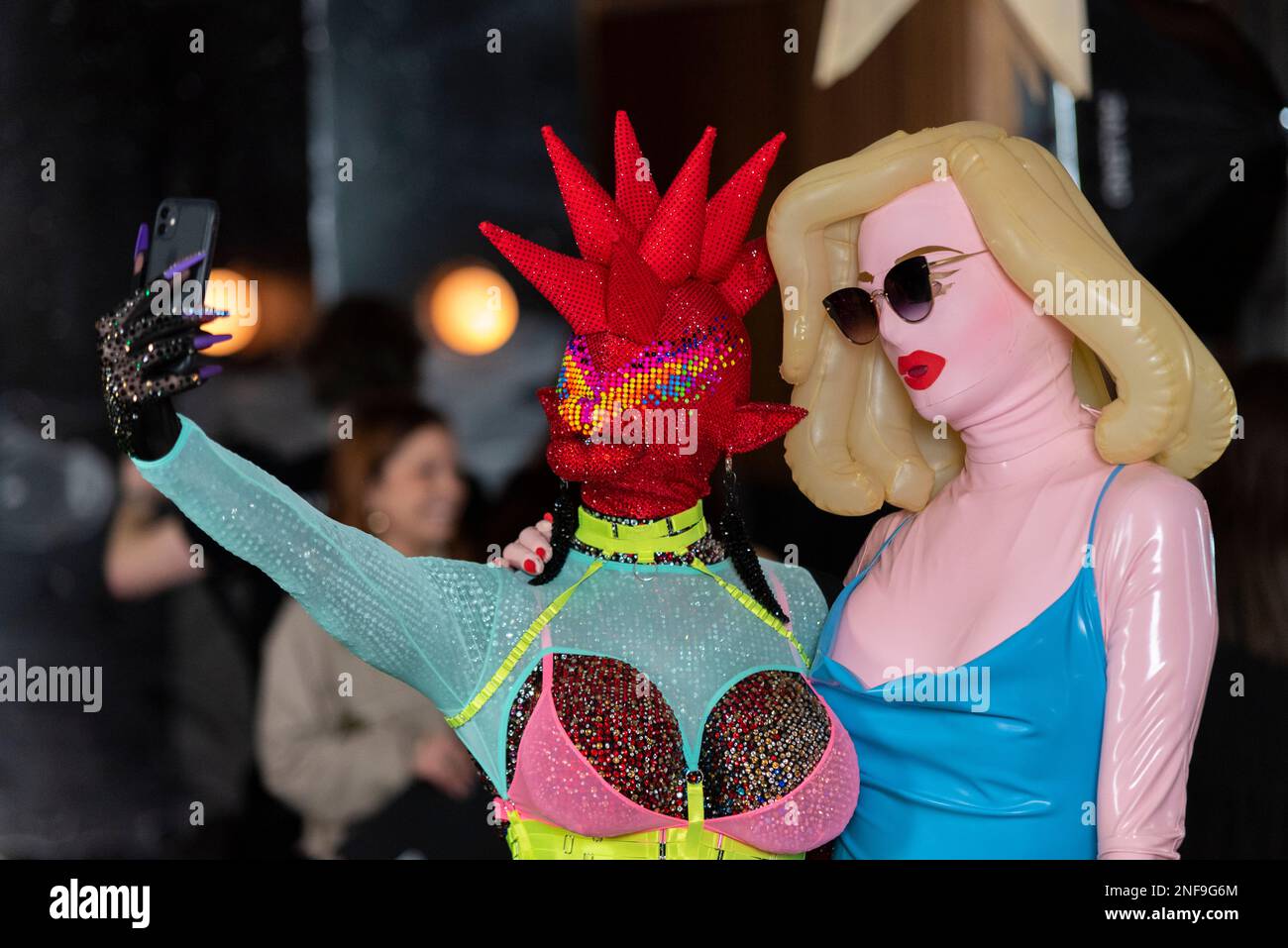 Guests at a VIN+OMI fashion show in outlandish masked costumes, taking a  selfie. One person in sequined outfit, one in latex doll style costume  Stock Photo - Alamy