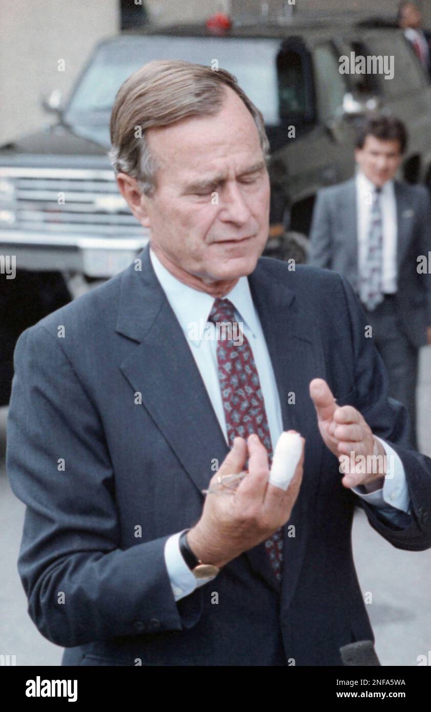 President George Bush holds up the bandaged middle finger of his right hand outsider Walter Reed Medical center in Washington, Oct. 7, 1989, after having a cyst surgically removed from the finger. The president said "all is well" to reporters outside the hospital after the hour-long operation before heading to Camp David, Md., for the weekend. (AP Photo/Barry Thumma) Stock Photo