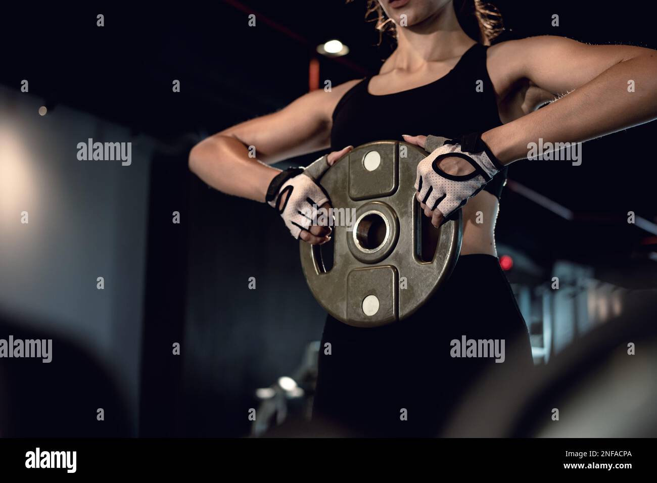 Sporty woman exercising with weight plate in the gym. Stock Photo