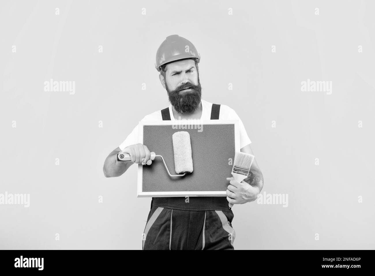 serious man renovator in helmet and work clothes hold paint roller