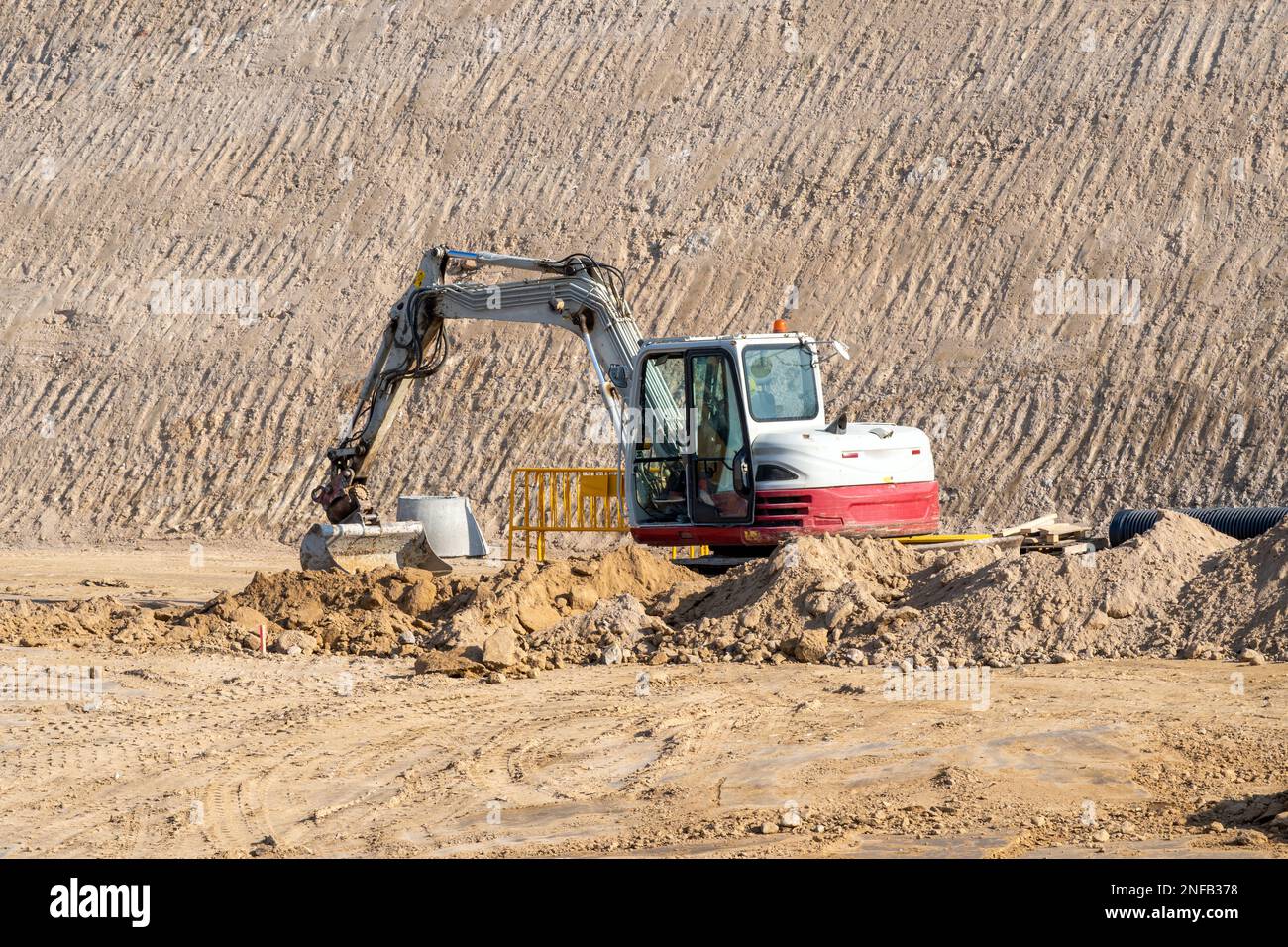 White and red small excavator moving earth in the middle of a large ...