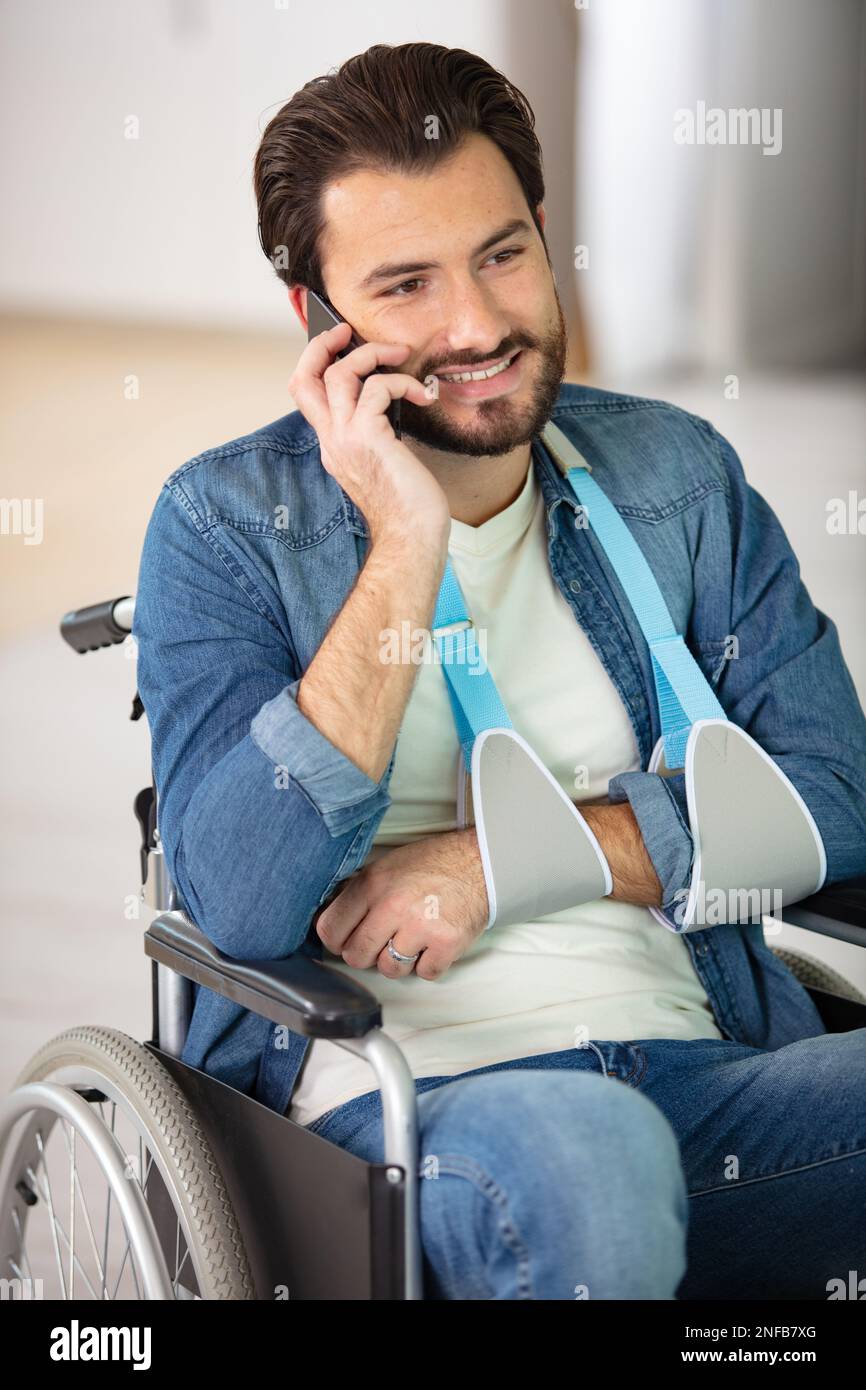 man in a wheelchair wearing a sling talking on telephone Stock Photo