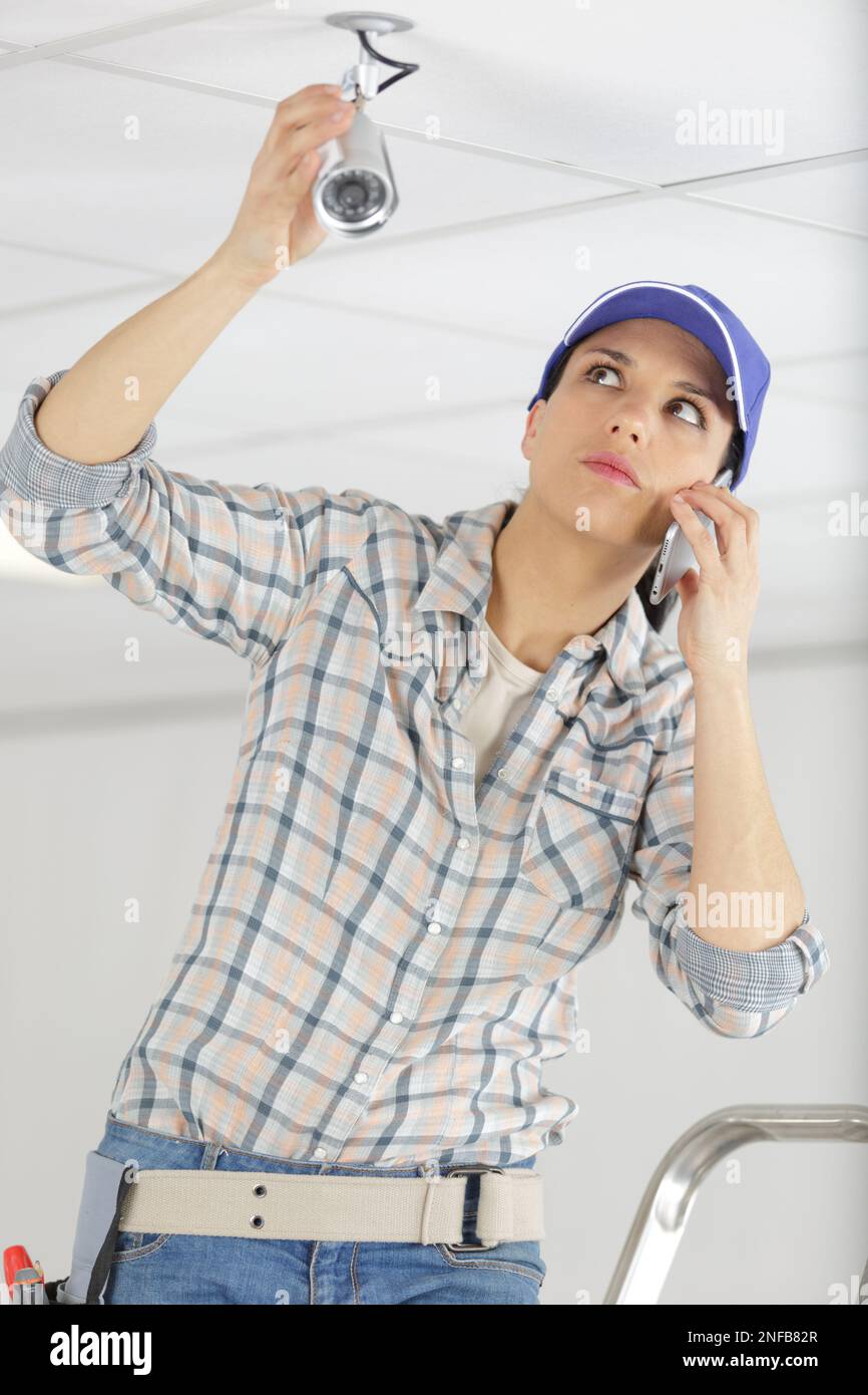 worried female technician using the phone while installing camera Stock Photo