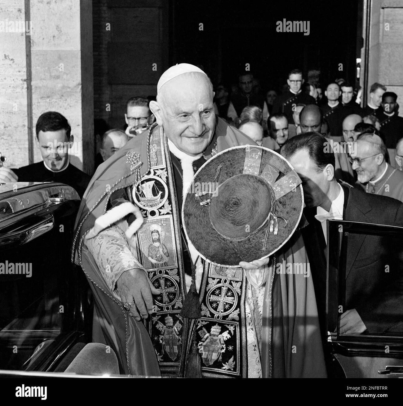 Pope John XXIII, in his papal robes and holding his hat, stands outside