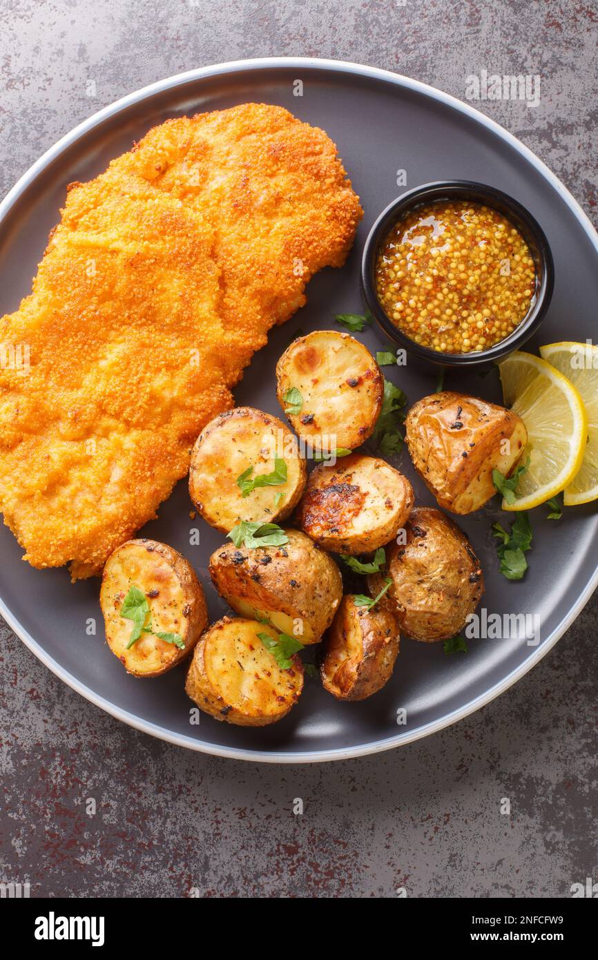 Munchner Schnitzel with baked potatoes and Dijon mustard closeup on the plate on the table. Vertical top view from above Stock Photo