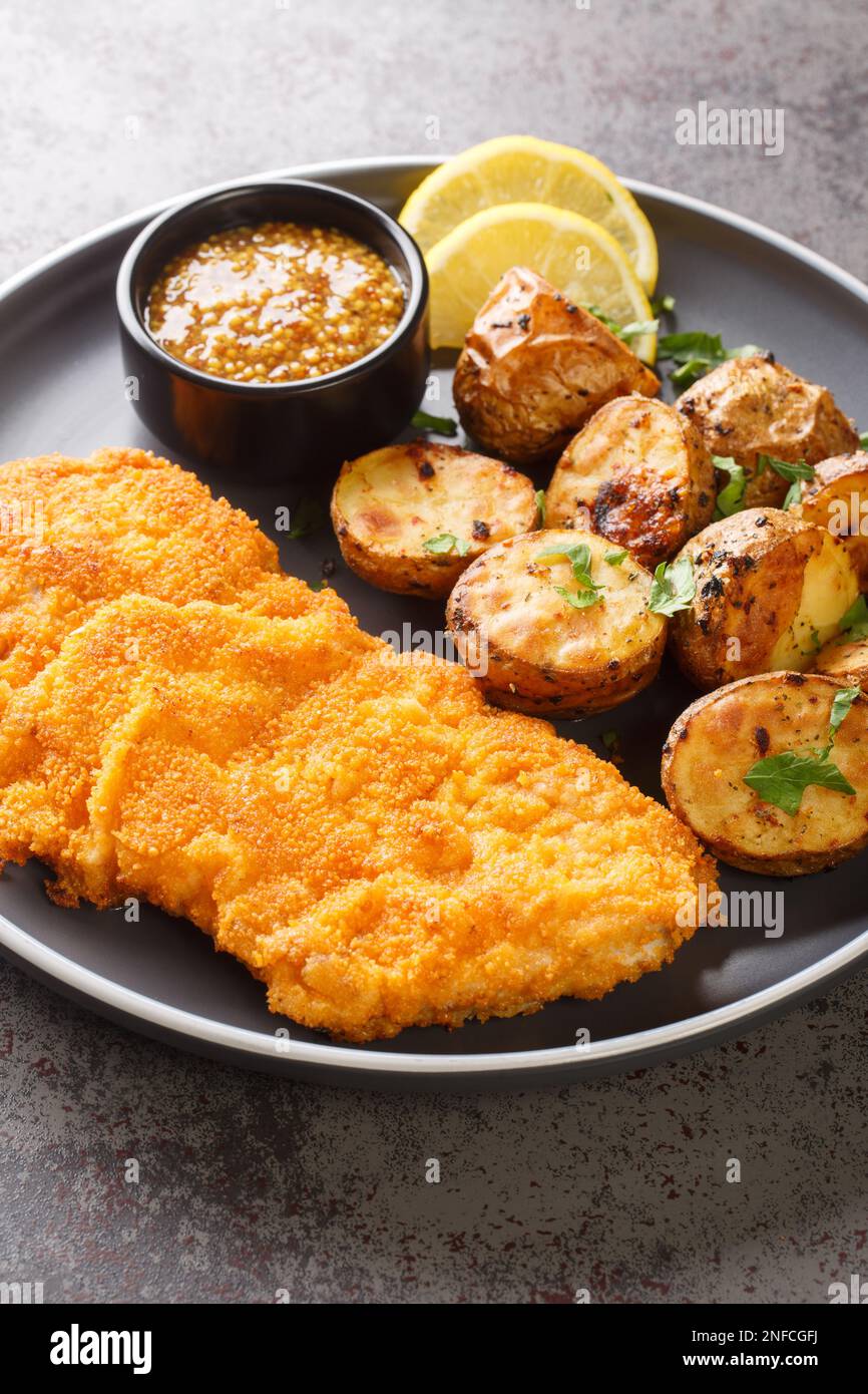 Munchner Schnitzel with baked potatoes and Dijon mustard closeup on the plate on the table. Vertical Stock Photo