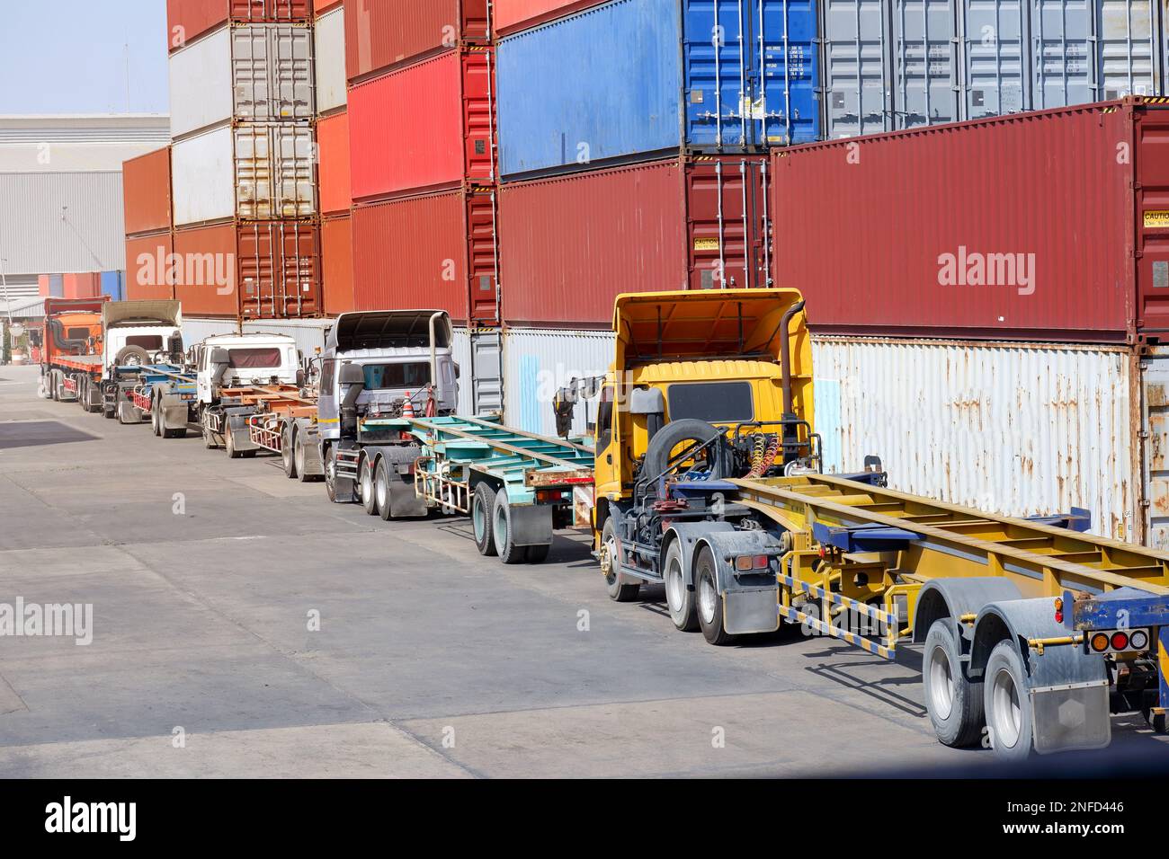 Trucks in a logistics yard with containers stacked in the background. Stock Photo