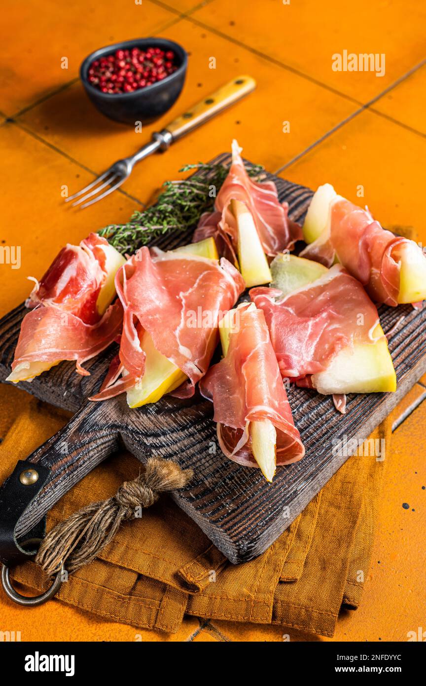 Prosciutto ham with slices of melon and fresh thyme. Orange background