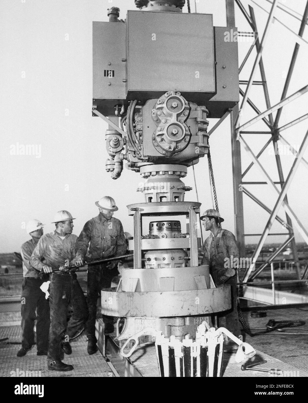 Unidentified oil fieldworkers fasten a blow-out preventer to a well ...