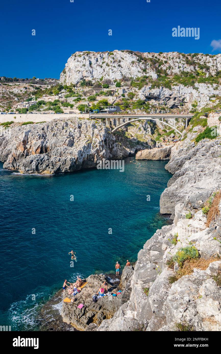 Agosto 17, 2022 - The Ciolo bridge, Gagliano del Capo. An inlet of the sea. The panorama of the splendid coast of Salento, Puglia. Some people swim in Stock Photo